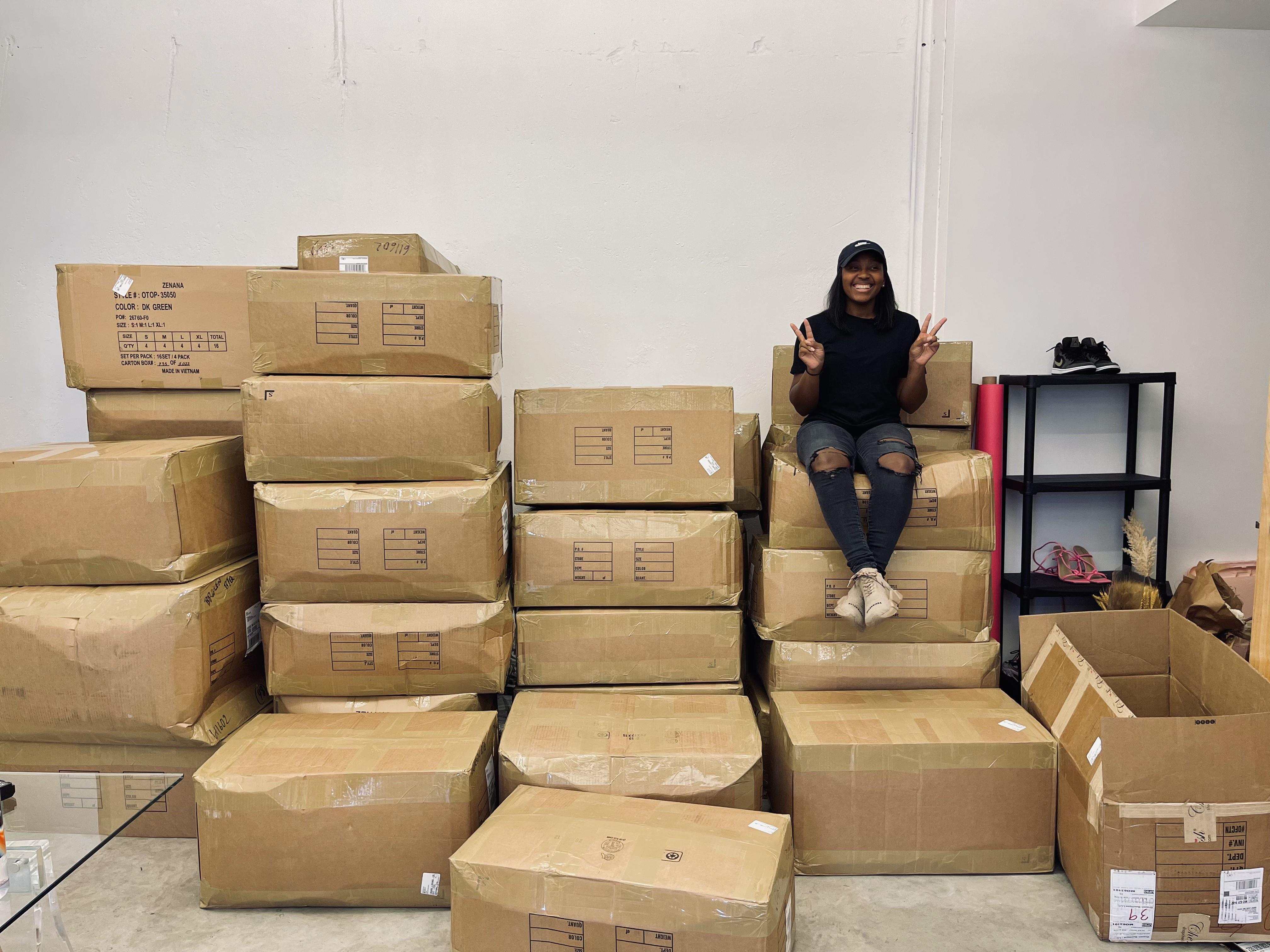 Jance with double peace signs on a tall stack of inventory boxes